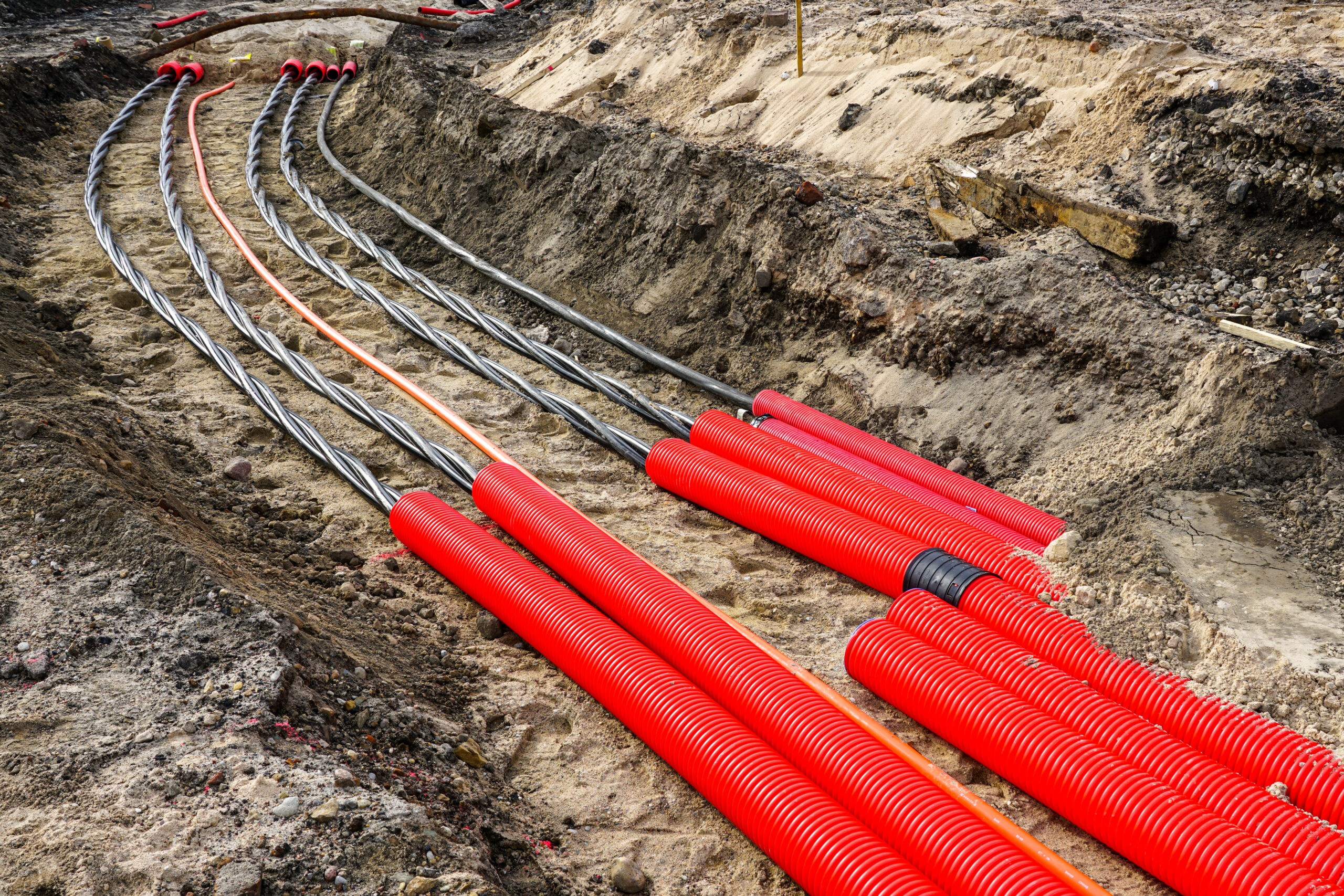 Underground electrical cable installation with red conduits laid in a trench at a construction site