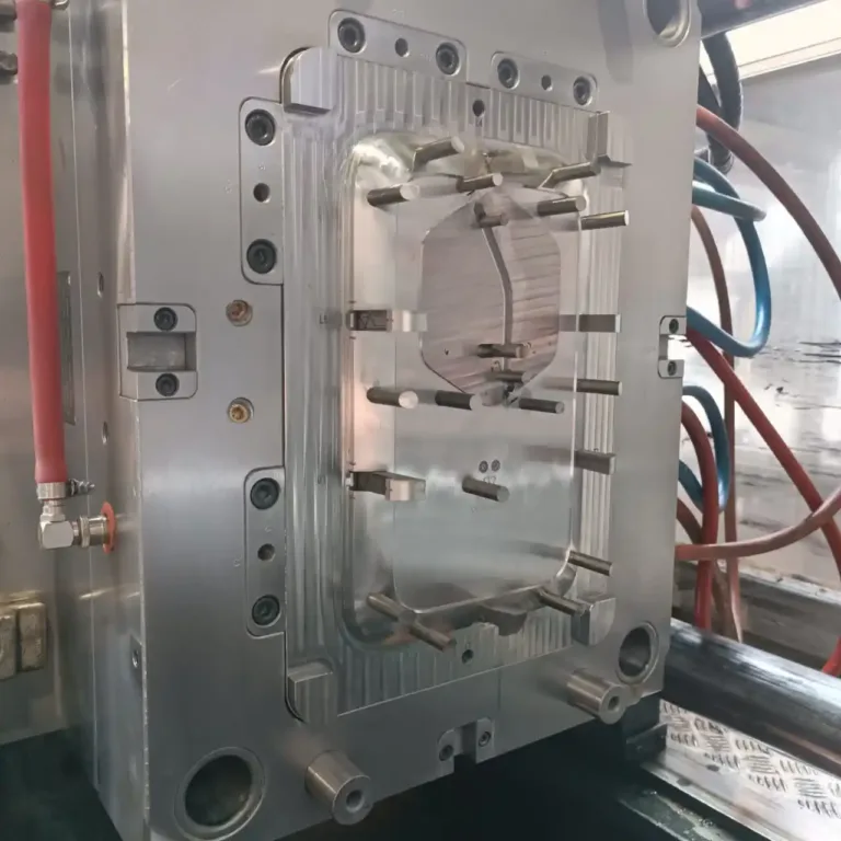 Close-up of a plastic injection mold with a circular cavity and multiple ejector pins around it, mounted in a metal frame with hoses nearby.