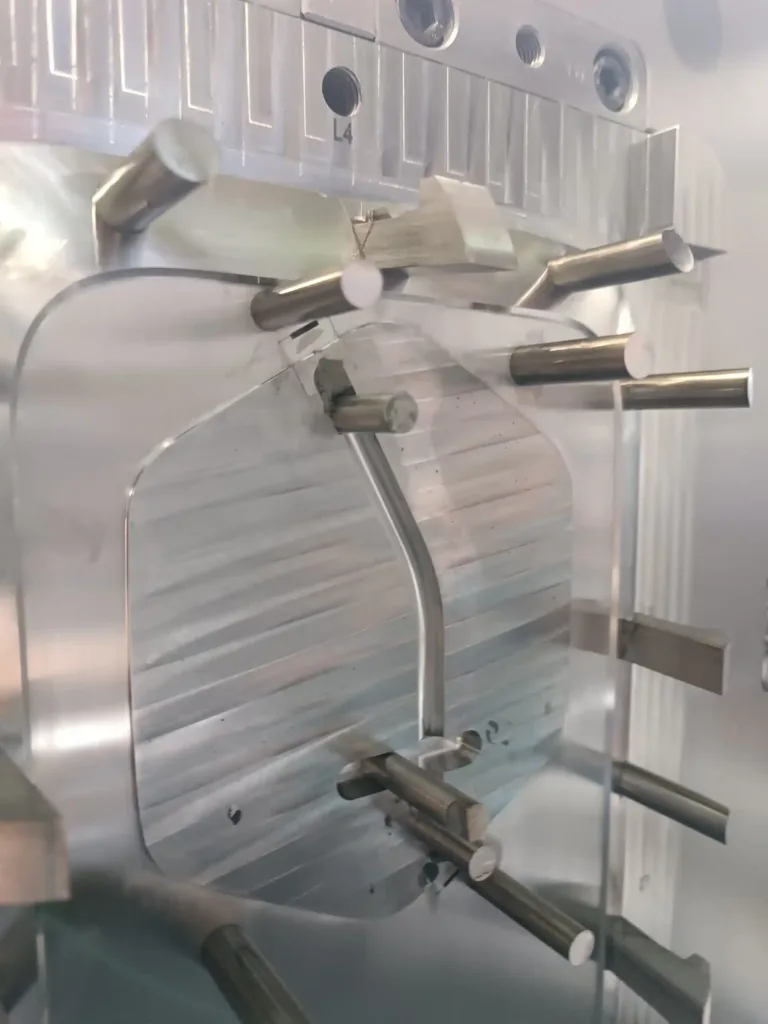 Close-up of a stainless steel fixture with cylindrical pins and clamps, labeled L4, holding metal parts in place.
