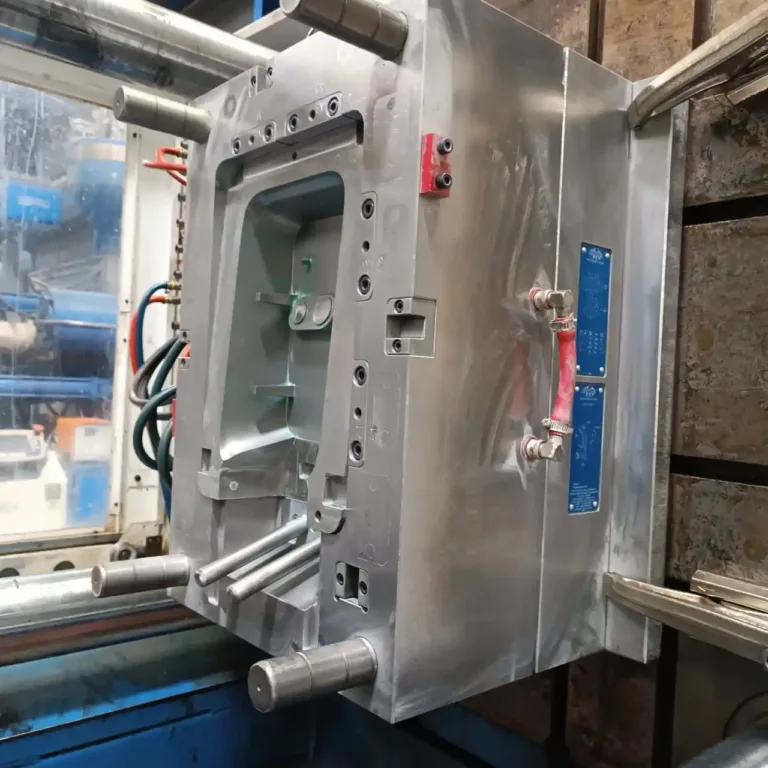 Industrial metal stamping die mounted in a hydraulic press, showing guide pins, clamp blocks, and hydraulic hoses in a manufacturing setting